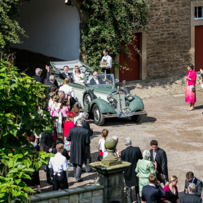 Oldtimer-Brautauto mit Brautpaar fährt in den Innenhof von Rittergut Remeringhausen. Gäste umstehen das Auto.