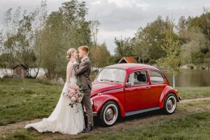 Brautpaar mit rotem VW Käfer auf der Teichwiese