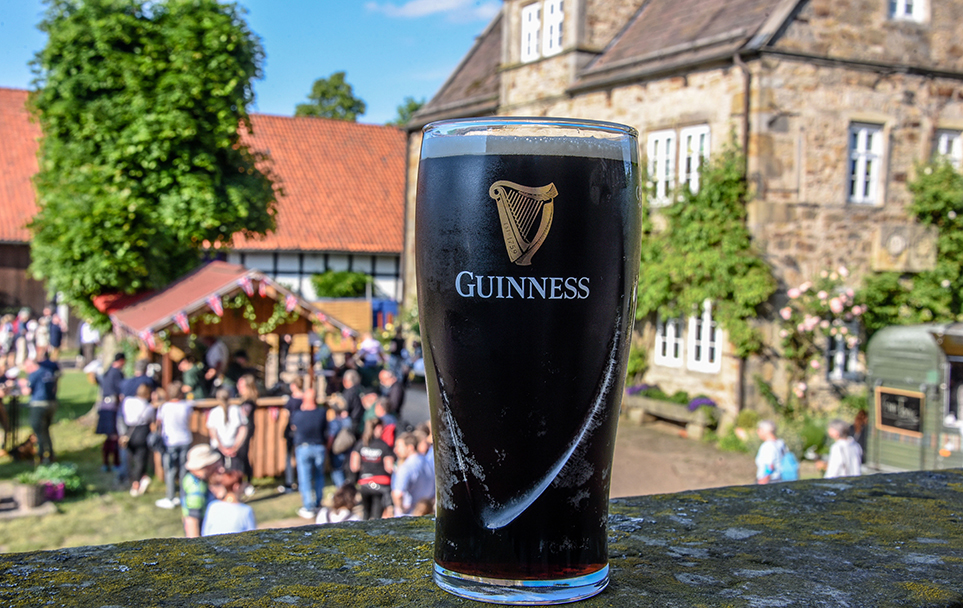 Ein Glas Guinness-Bier im Vordergrund vor dem bunten Treiben des British Weekend.