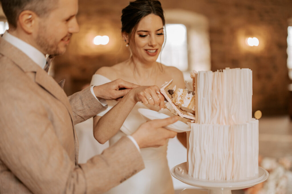 Hochzeitsshooting im Torhaus RIttergut Remeringhausen - Brautpaar steht vor der Hochzeitstorte mit Kuchenstück