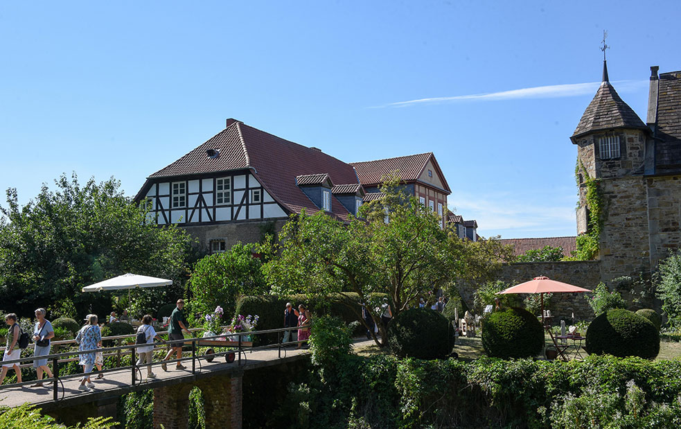 Blick vom Park Richtung Innenhof von Rittergut Remeringhausen - Besucher flanieren über die Brücke beim Romantic Garden